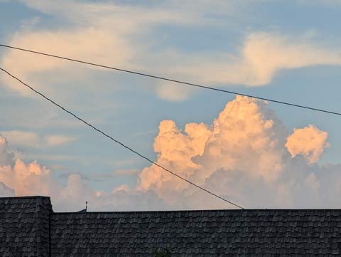A sunlit cloud against a blue sky on a sunny day, looming over a roof top