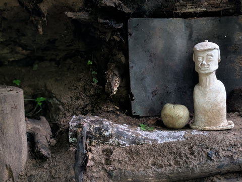 A bust of a man, resembling Salvador Dali, perched on an earthen shelf in a makeshift hut