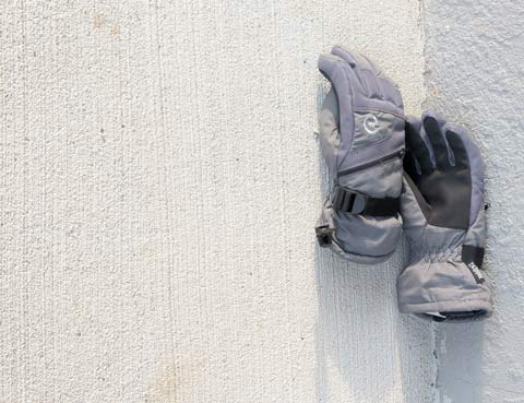 A pair of Winter gloves laying on a concrete walkway along a white stucco wall