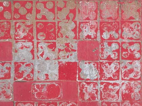 A grid pattern on a red wall, made by the pain that is missing from the wall from when tiles were removed from it.