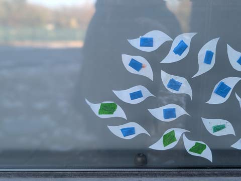 A group of leaves cut out of paper taped to a window with blue and green tape