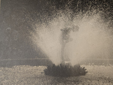 A photo of a black and white photo of a young girl, or maybe a statue of a your girl, standing in the middle of a fountain