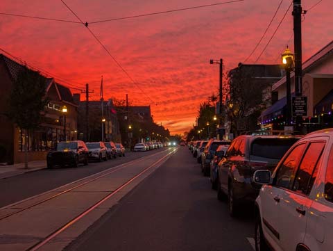 A red sky at the end of the day over a main street in a small suburban town. The red reflecting off of the cars lines up along the street