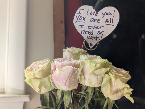 A half dozen gold roses, with blush colored centers and outer petals tinged with a light green. There is a heart shaped note that reads "I love you. You are all I ever need or want! —M" sticking out of the bunch