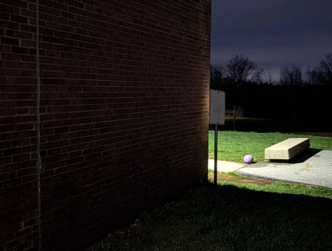 A bright light in the darkness illuminating a purple ball and a long rectangular cement slab bench