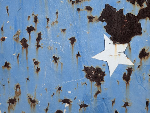 A white star painted on a blue field that is spotted with spots of rust