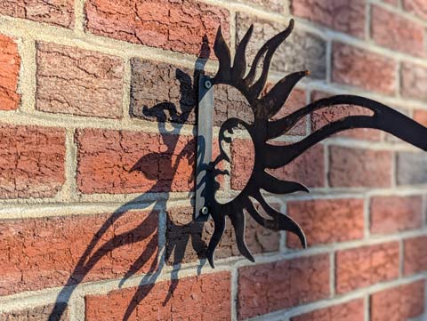 A shadow of a plant hanger on a brick wall that forms the shape of a smiling sun