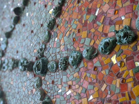 Green ceramic tiles in the shape of heads, snaking into the distance on a bed of red and orange tiles
