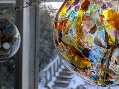 A witch ball hanging in front of a bow window with light from a seeting sun reflecting on it